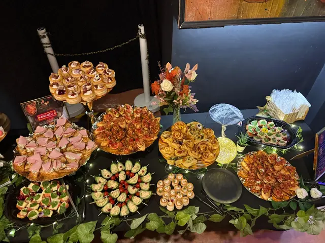 Masa festiva cu etajere de aperitive, platouri reci si flori, intr-o sala de seara