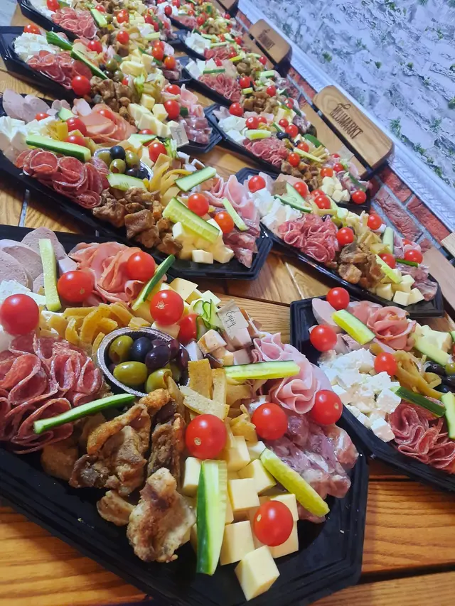 Mai multe platouri de charcuterie si legume proaspete, aliniate pe o masa de lemn